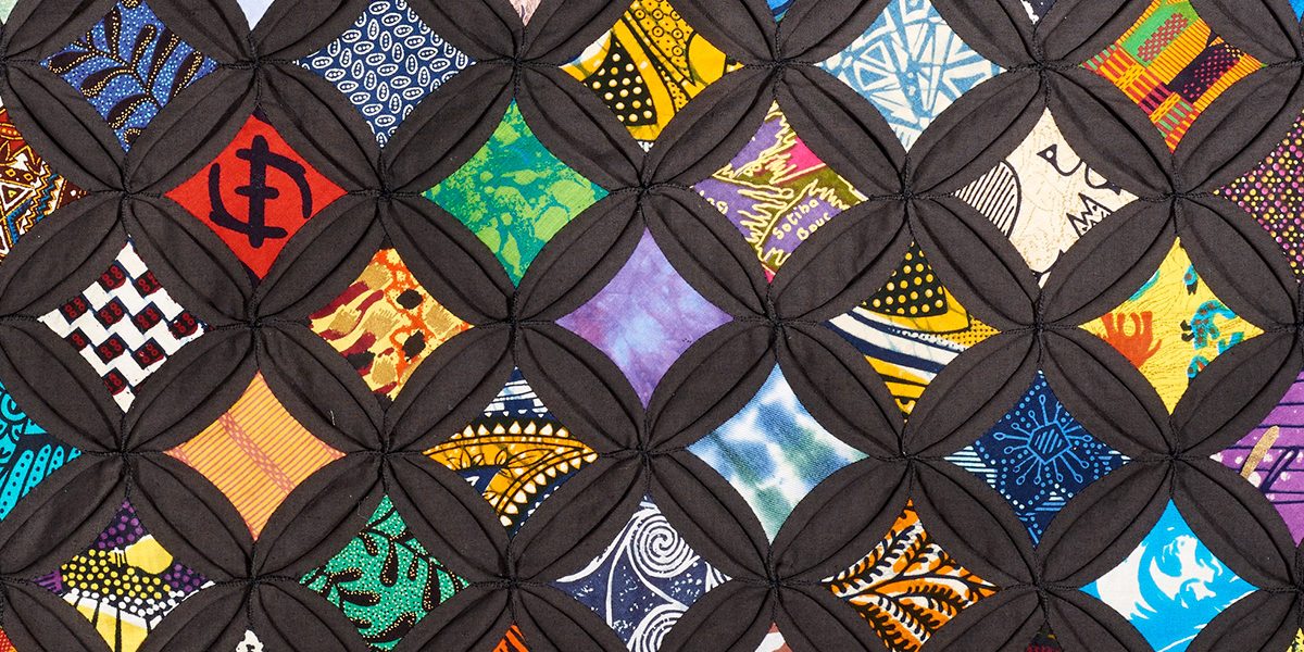 Viola Canady’s colorful quilt, with bright patterned fabric set in a black, cathedral-window grid.