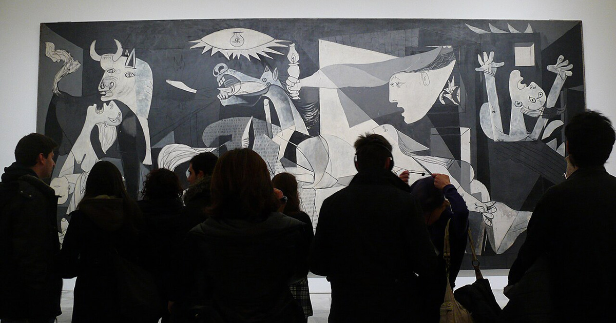 A wide shot inside a well-lit museum gallery where a crowd of people stands in front of Pablo Picasso's massive anti-war painting, Guernica. The viewers are seen from behind as dark silhouettes, looking up at the monumental black, white, and gray canvas that stretches across most of the white wall. The painting itself is filled with fractured, cubist figures expressing agony and chaos, including a screaming horse, a bull, a crying mother holding a child, and a large eye-like lightbulb at the top center. The lower right corner of the photograph contains overlapping translucent text blocks from a web browser download menu, covering a small portion of the crowd.